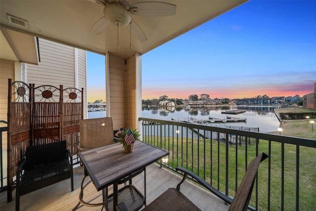 balcony at dusk with a water view, ceiling fan, and visible vents