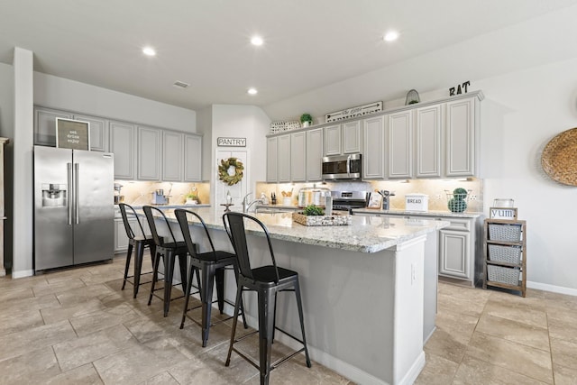 kitchen featuring light stone countertops, a breakfast bar, a kitchen island with sink, appliances with stainless steel finishes, and tasteful backsplash