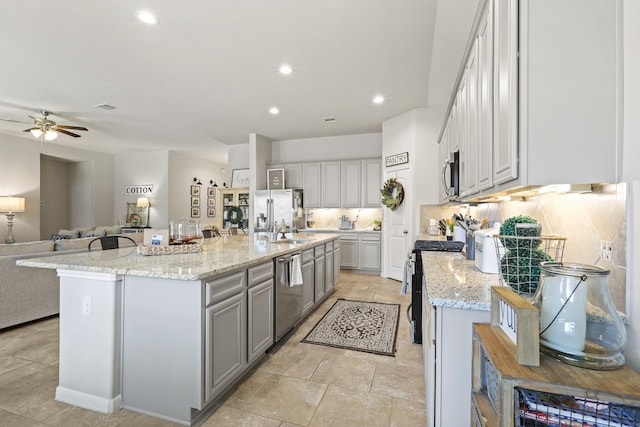 kitchen with gray cabinets, a sink, stainless steel appliances, open floor plan, and backsplash