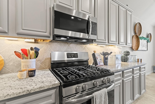 kitchen with gray cabinetry, light stone counters, appliances with stainless steel finishes, decorative backsplash, and baseboards