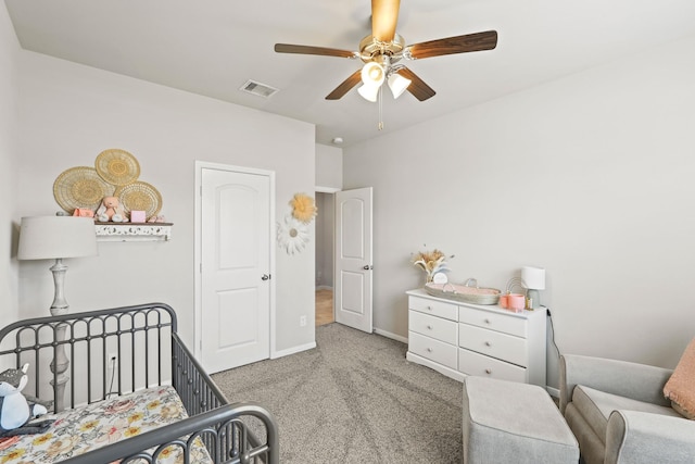 carpeted bedroom with visible vents, baseboards, a nursery area, and a ceiling fan