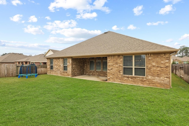 rear view of house with a patio, a trampoline, a fenced backyard, a yard, and brick siding