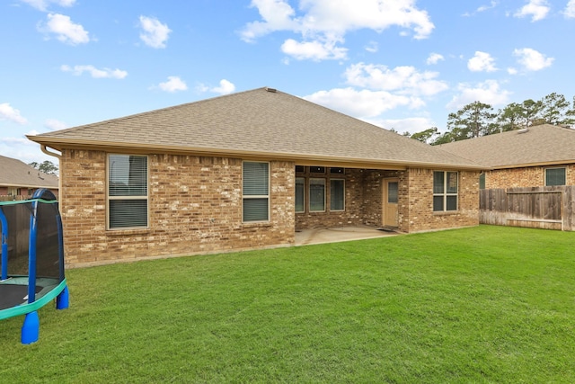 rear view of property with fence, a shingled roof, a trampoline, a patio area, and brick siding