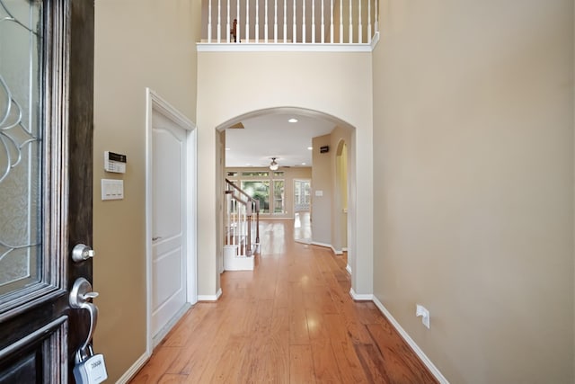 foyer entrance featuring arched walkways, stairway, light wood-style flooring, ceiling fan, and baseboards