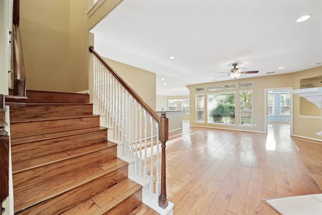 stairs with baseboards, ceiling fan with notable chandelier, wood finished floors, and recessed lighting