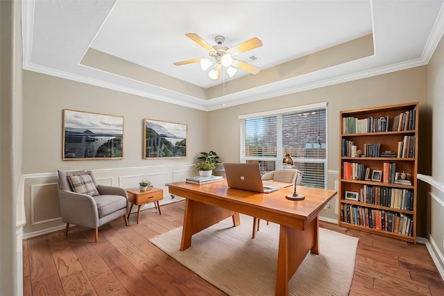 office with a decorative wall, a raised ceiling, a ceiling fan, and light wood-style floors