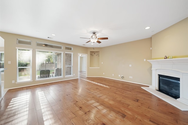 unfurnished living room with light wood-style flooring, baseboards, ceiling fan, and a glass covered fireplace