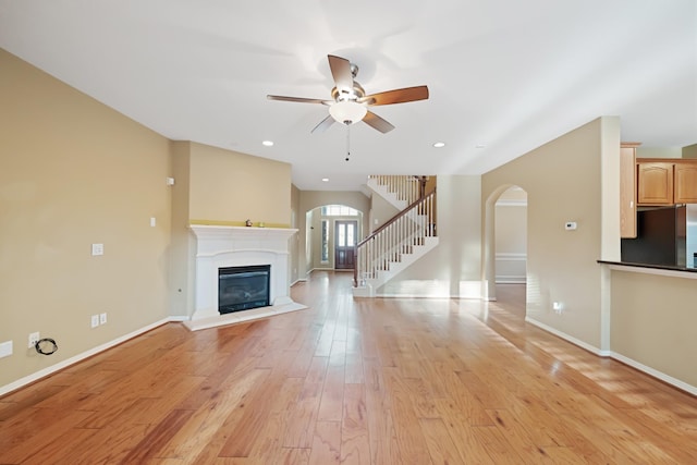 unfurnished living room featuring arched walkways, stairway, light wood-type flooring, and baseboards