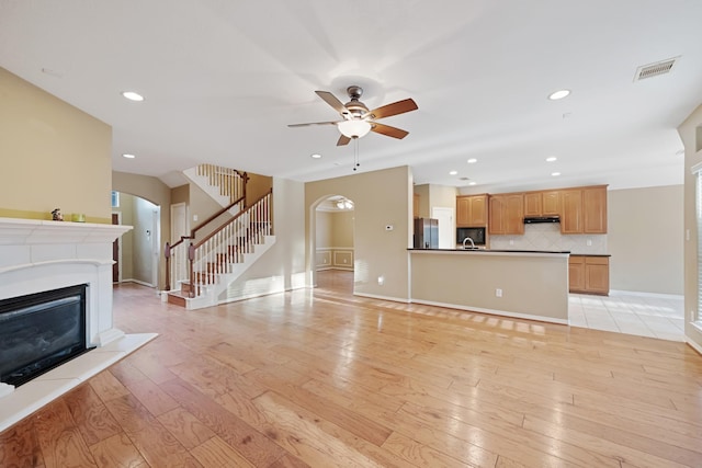 unfurnished living room with stairway, visible vents, arched walkways, and a glass covered fireplace