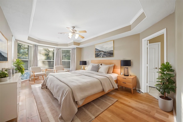 bedroom with ceiling fan, a tray ceiling, light wood-style flooring, and crown molding