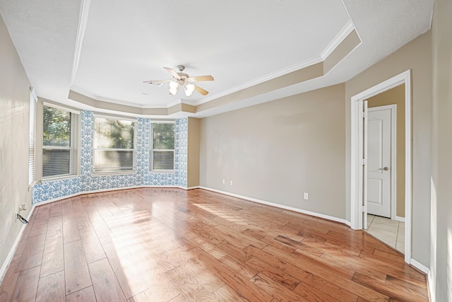 spare room with baseboards, a tray ceiling, light wood-type flooring, and crown molding