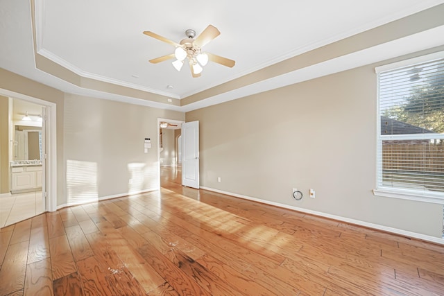 unfurnished room featuring ceiling fan, baseboards, light wood-style floors, a raised ceiling, and crown molding