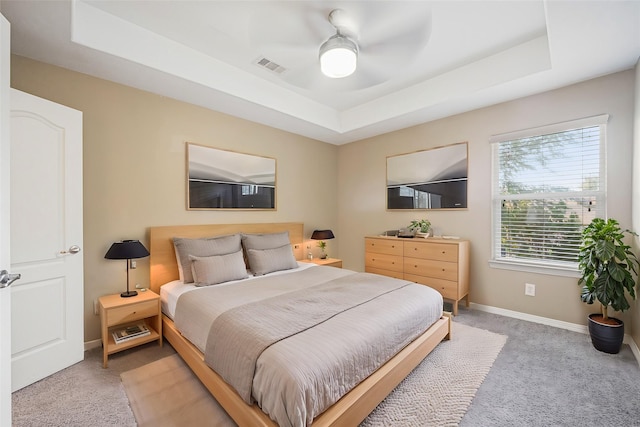 bedroom with light colored carpet, a tray ceiling, visible vents, and baseboards