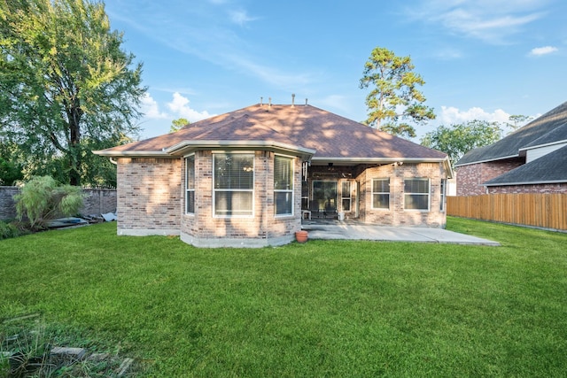 rear view of property featuring brick siding, a patio, a shingled roof, a lawn, and fence