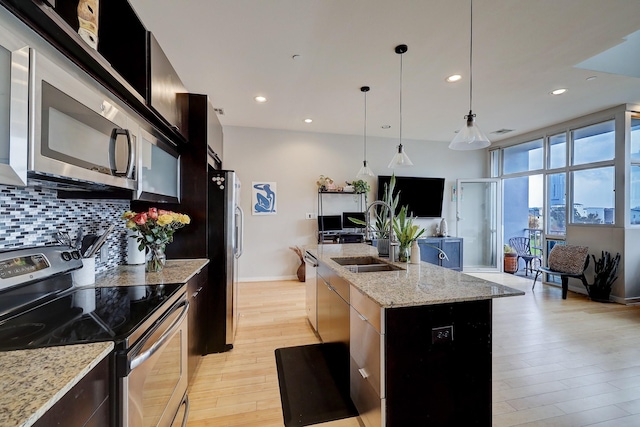 kitchen featuring a kitchen island with sink, stainless steel appliances, light wood-style floors, backsplash, and modern cabinets