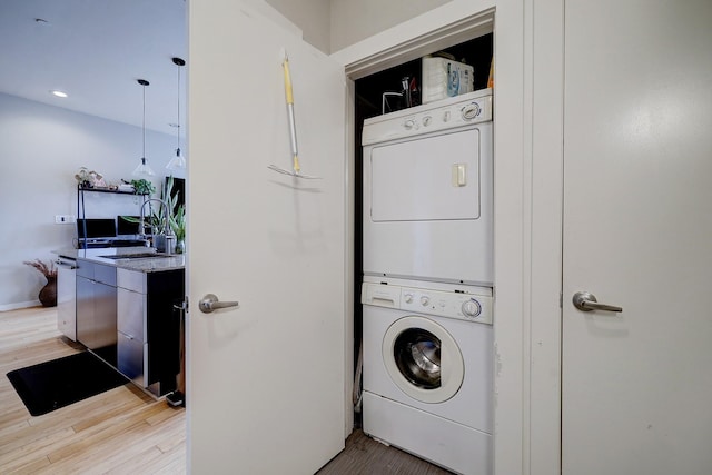 laundry room with stacked washer and clothes dryer, recessed lighting, wood finished floors, laundry area, and baseboards