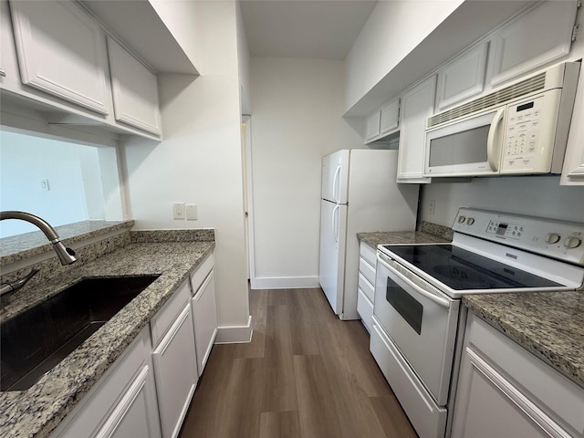 kitchen featuring dark wood-type flooring, stone countertops, a sink, white appliances, and baseboards