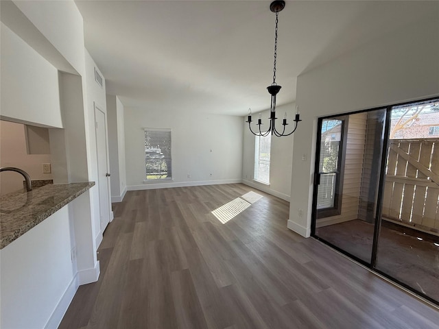 unfurnished dining area featuring a chandelier, visible vents, baseboards, and wood finished floors