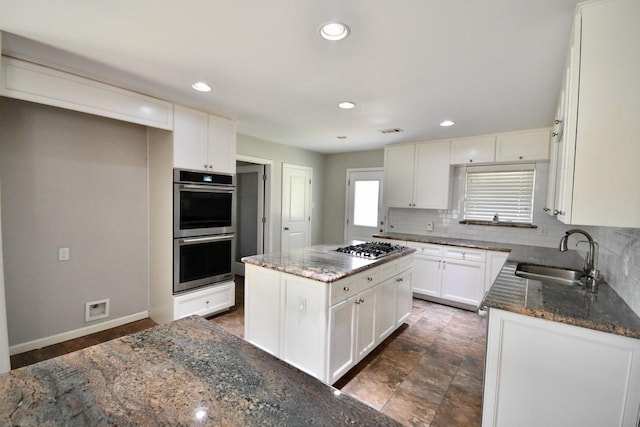 kitchen featuring appliances with stainless steel finishes, dark stone countertops, a sink, and decorative backsplash