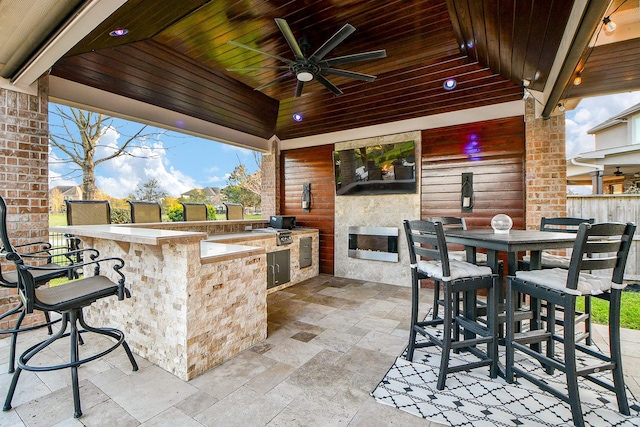 view of patio featuring outdoor dining space, a ceiling fan, fence, outdoor wet bar, and an outdoor kitchen