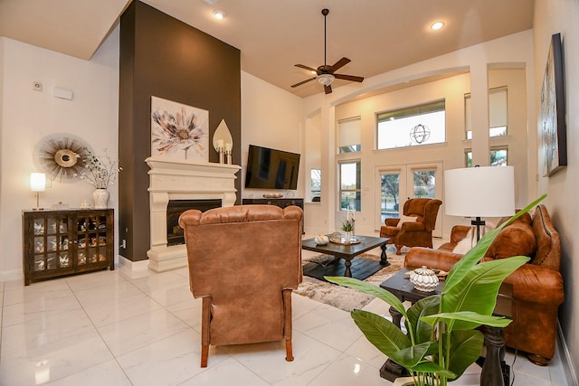 living room featuring a ceiling fan, baseboards, a high ceiling, a fireplace with raised hearth, and marble finish floor