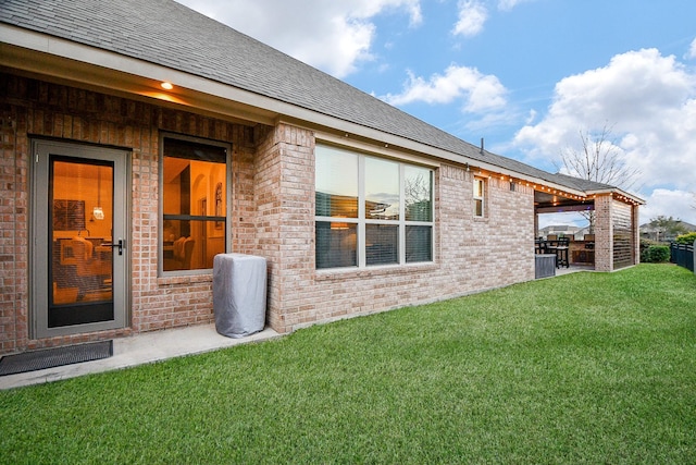 back of house featuring a patio, a lawn, brick siding, and roof with shingles