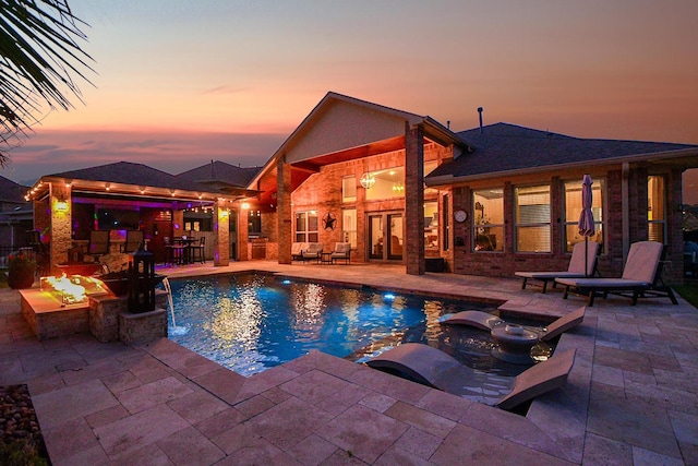 pool at dusk with a patio and an outdoor pool