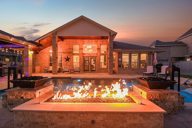 back of property at dusk with a patio area, a fire pit, and an outdoor pool