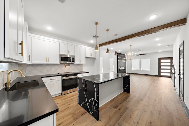 kitchen with light wood-style flooring, a sink, appliances with stainless steel finishes, beamed ceiling, and dark countertops