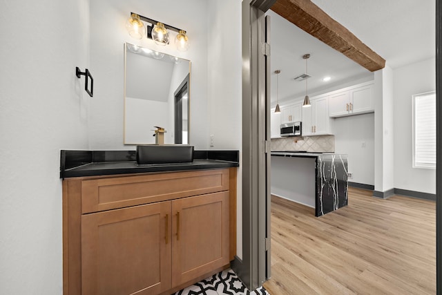 bathroom featuring wood finished floors, vanity, baseboards, beam ceiling, and decorative backsplash