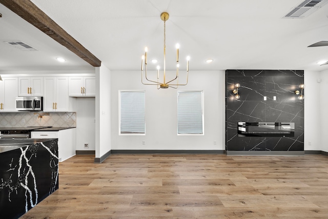 kitchen featuring light wood-style flooring, stainless steel microwave, visible vents, and decorative backsplash