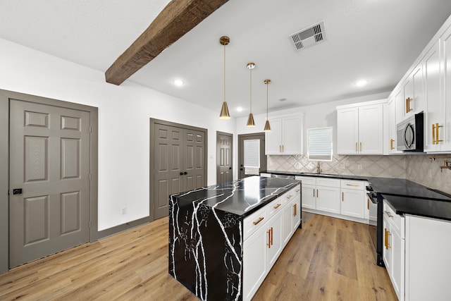 kitchen featuring light wood finished floors, visible vents, dark countertops, stainless steel microwave, and backsplash