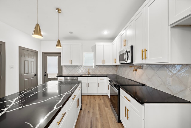 kitchen with light wood-style flooring, a sink, appliances with stainless steel finishes, backsplash, and dark countertops