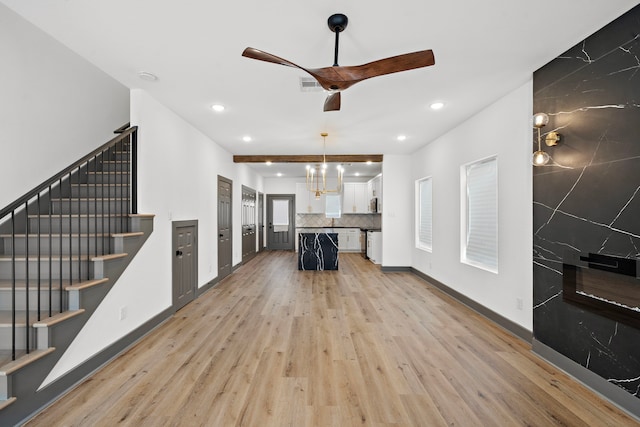 unfurnished living room with stairs, visible vents, light wood-style flooring, baseboards, and ceiling fan with notable chandelier