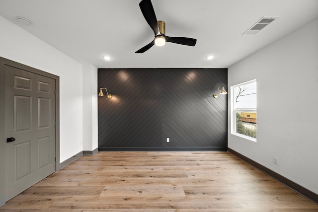 empty room with an accent wall, light wood finished floors, visible vents, and baseboards