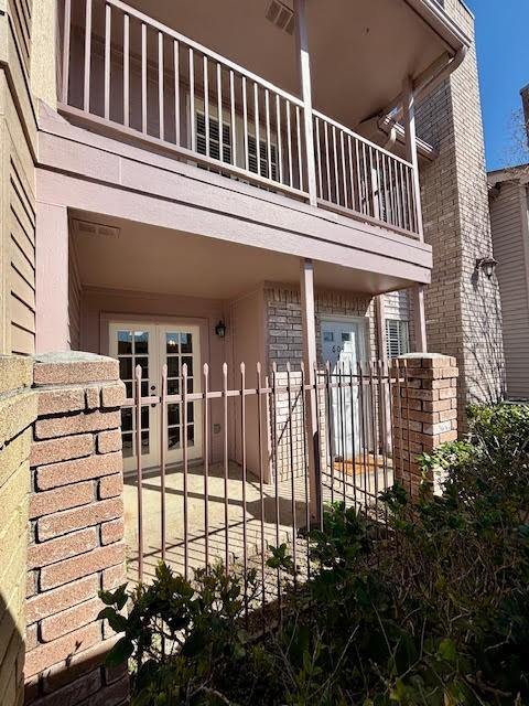 exterior space with french doors, brick siding, fence, and a balcony