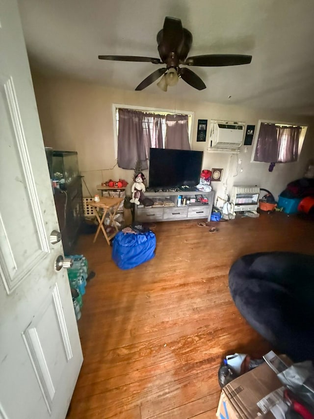 living room with ceiling fan, an AC wall unit, and wood finished floors