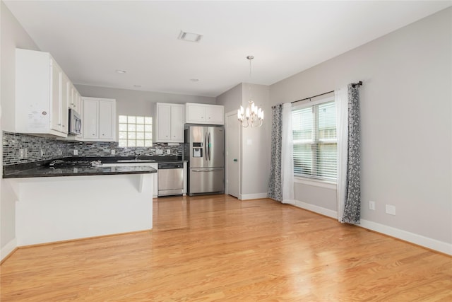 kitchen with dark countertops, backsplash, appliances with stainless steel finishes, a sink, and a peninsula