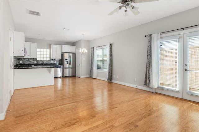 unfurnished living room with ceiling fan with notable chandelier, visible vents, baseboards, french doors, and light wood finished floors