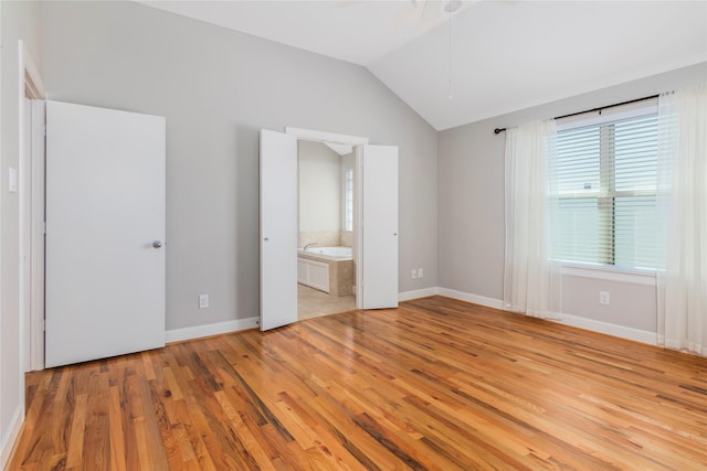 unfurnished bedroom featuring lofted ceiling, light wood-style floors, baseboards, and connected bathroom