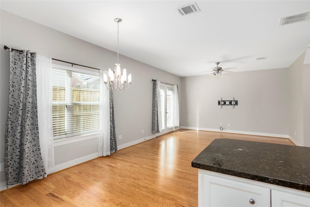 unfurnished dining area with ceiling fan with notable chandelier, light wood-style flooring, visible vents, and baseboards