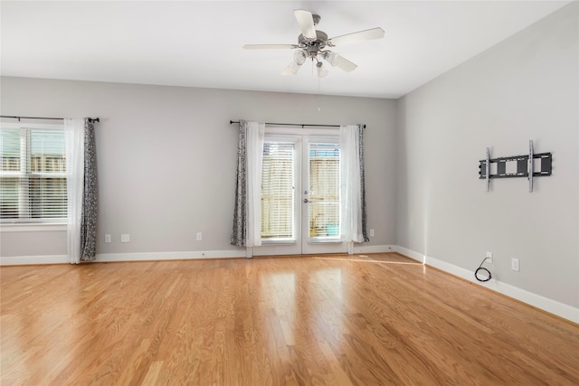 spare room featuring a ceiling fan, light wood-type flooring, a healthy amount of sunlight, and baseboards