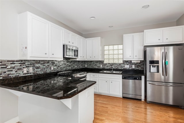 kitchen with appliances with stainless steel finishes, white cabinets, a sink, and a peninsula