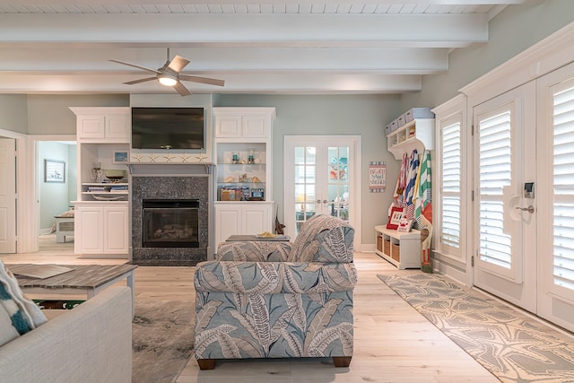 living room with french doors, light wood-type flooring, a glass covered fireplace, and beam ceiling