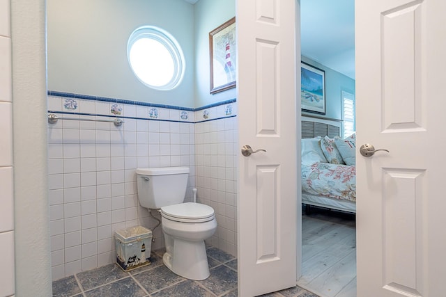 ensuite bathroom with toilet, a wainscoted wall, tile walls, and ensuite bathroom