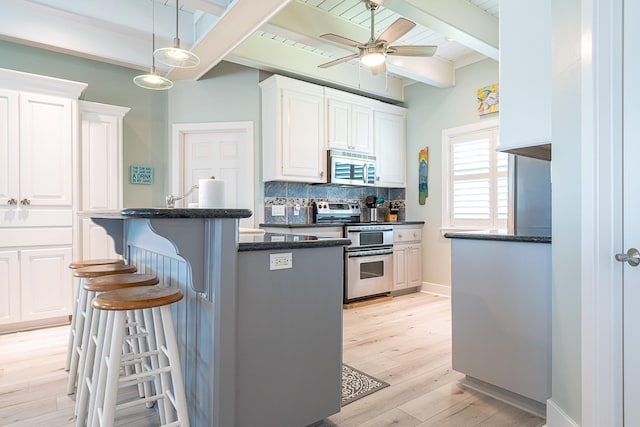 kitchen featuring stainless steel appliances, white cabinetry, a kitchen breakfast bar, backsplash, and beamed ceiling