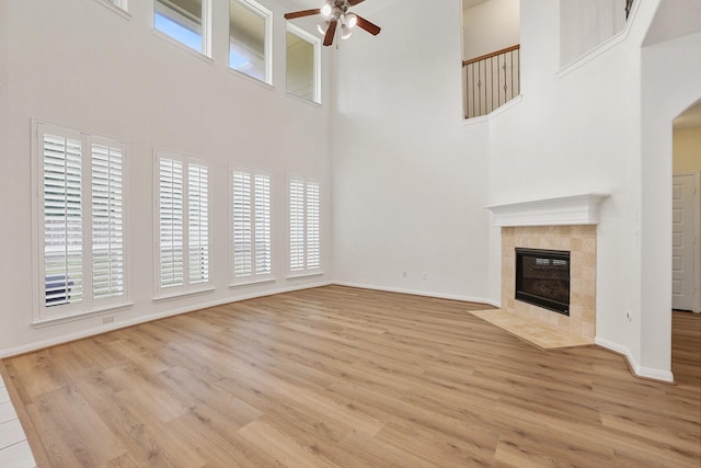 unfurnished living room featuring baseboards, ceiling fan, a tiled fireplace, and wood finished floors