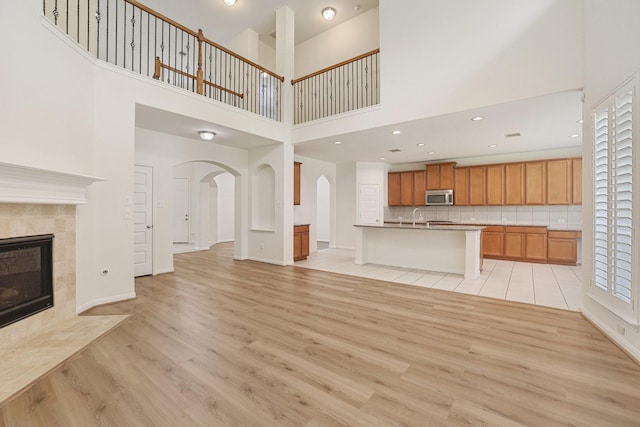 unfurnished living room featuring arched walkways, a sink, a healthy amount of sunlight, light wood-type flooring, and a tiled fireplace