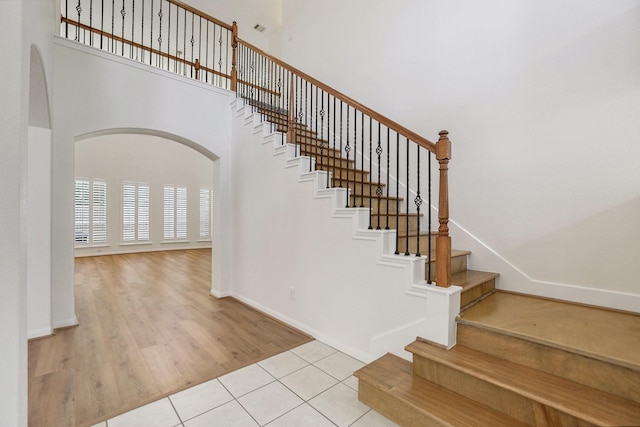 stairway featuring baseboards, a high ceiling, arched walkways, and tile patterned floors