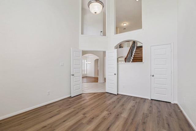 spare room featuring baseboards, arched walkways, a towering ceiling, stairway, and wood finished floors